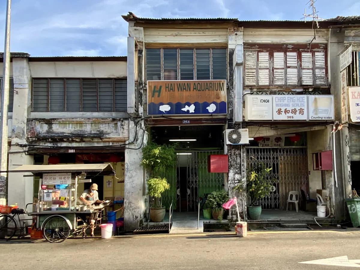A row of two-storey heritage shophouses with shuttered windows on Beach Street in George Town, Penang, with a street hawker cart outside