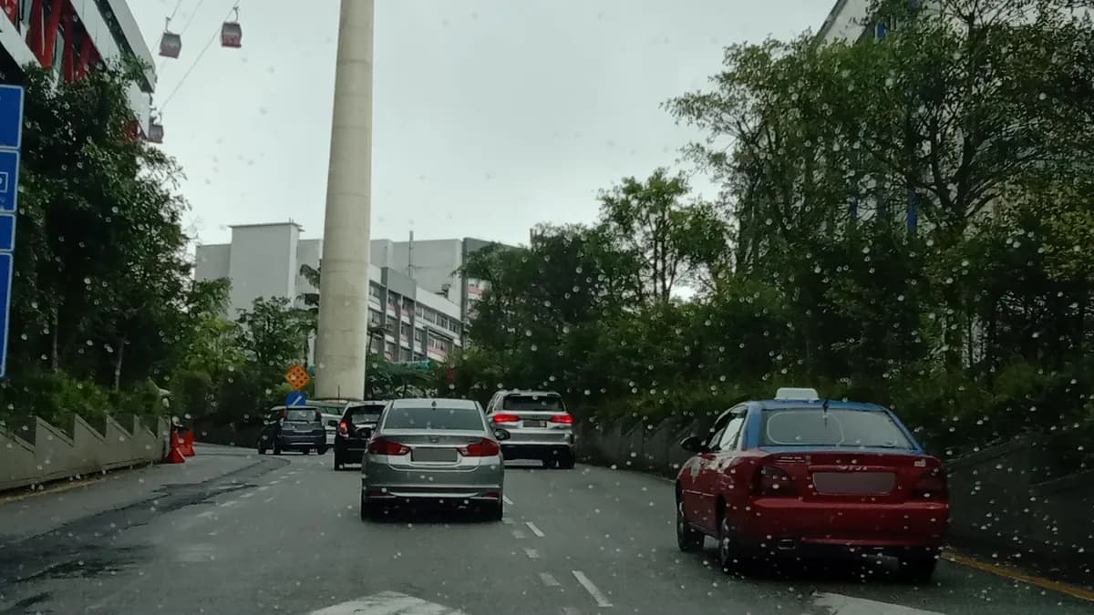 Rain streaking a windscreen on the road up to Genting Highlands, with cars ahead and cable-car gondolas passing overhead