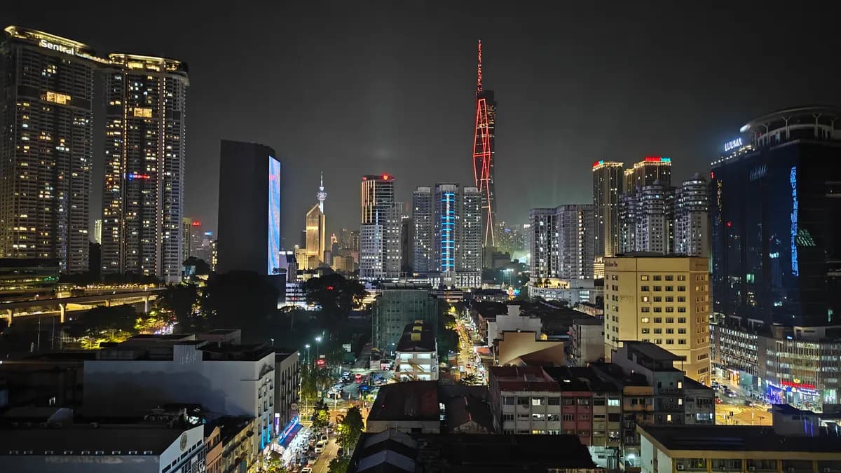 Kuala Lumpur after dark, with the lit Merdeka 118 tower and KL Tower rising above the rooftops and streets of the Brickfields area near KL Sentral