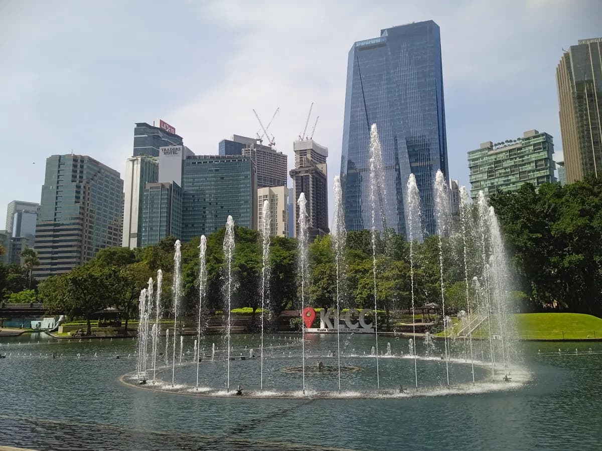 The fountains of the KLCC Park lake in front of the KLCC sign, with office towers and construction cranes of central Kuala Lumpur behind