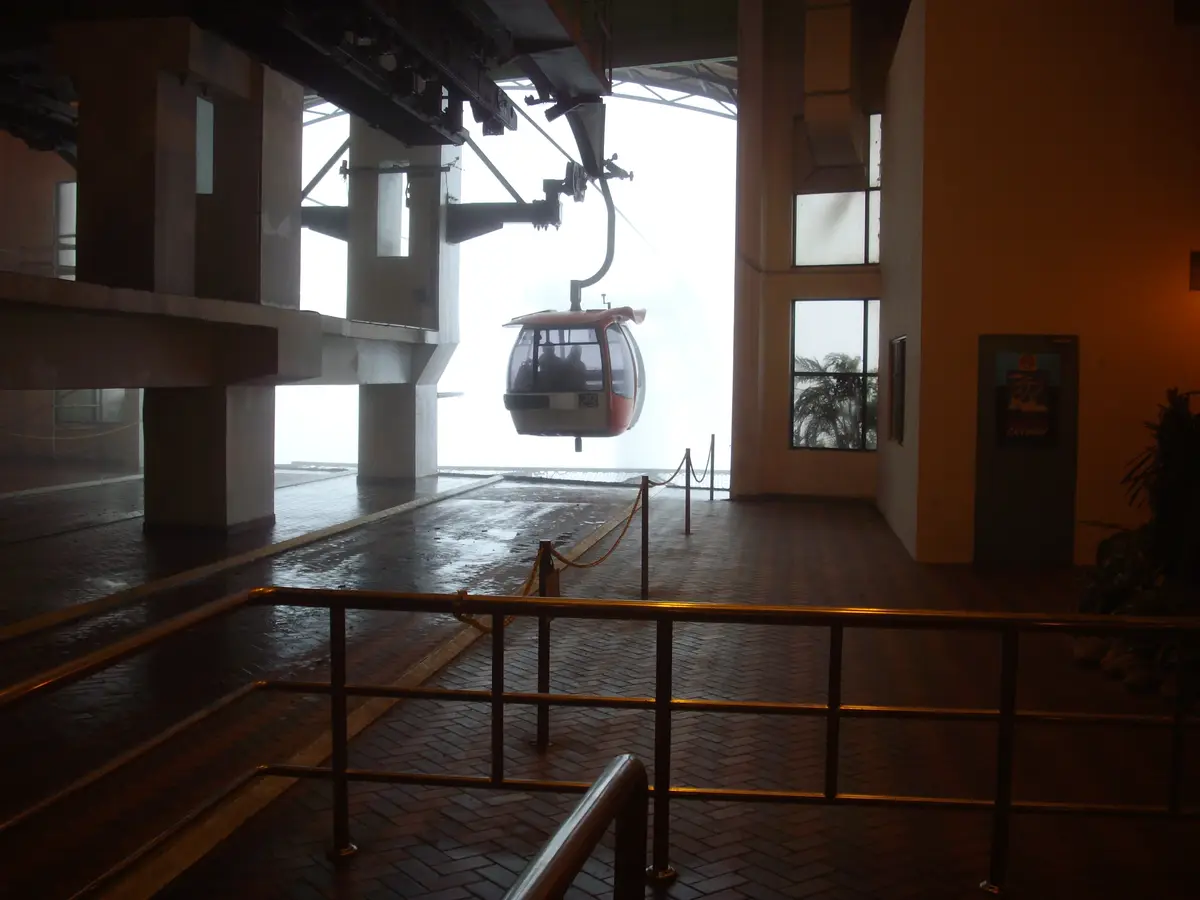 A cable car gondola arrives at a misty station building in Genting Highlands, with a railing and a wet brick floor in the foreground