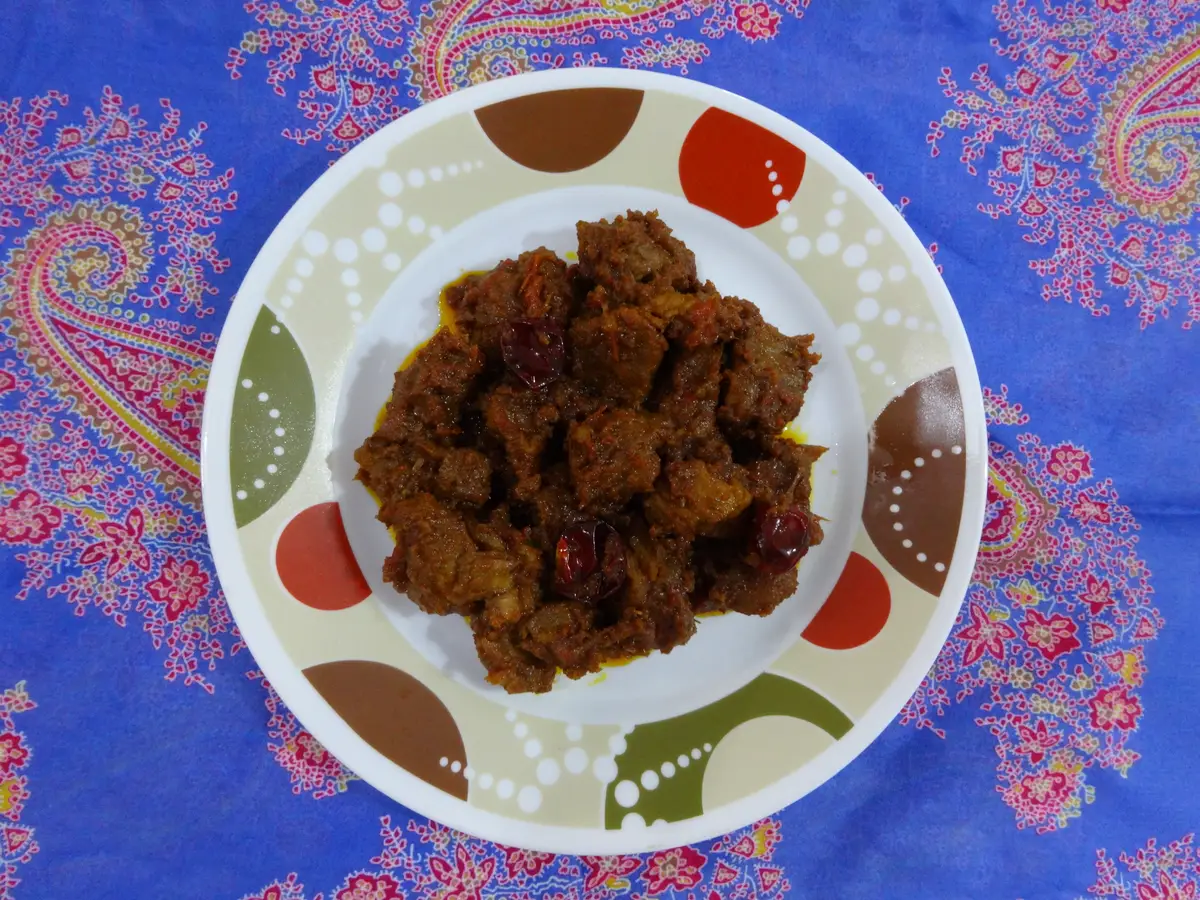 A round plate of beef rendang seen from above: dark, rich chunks of slow-cooked beef coated in a thick spice paste with dried red chilies
