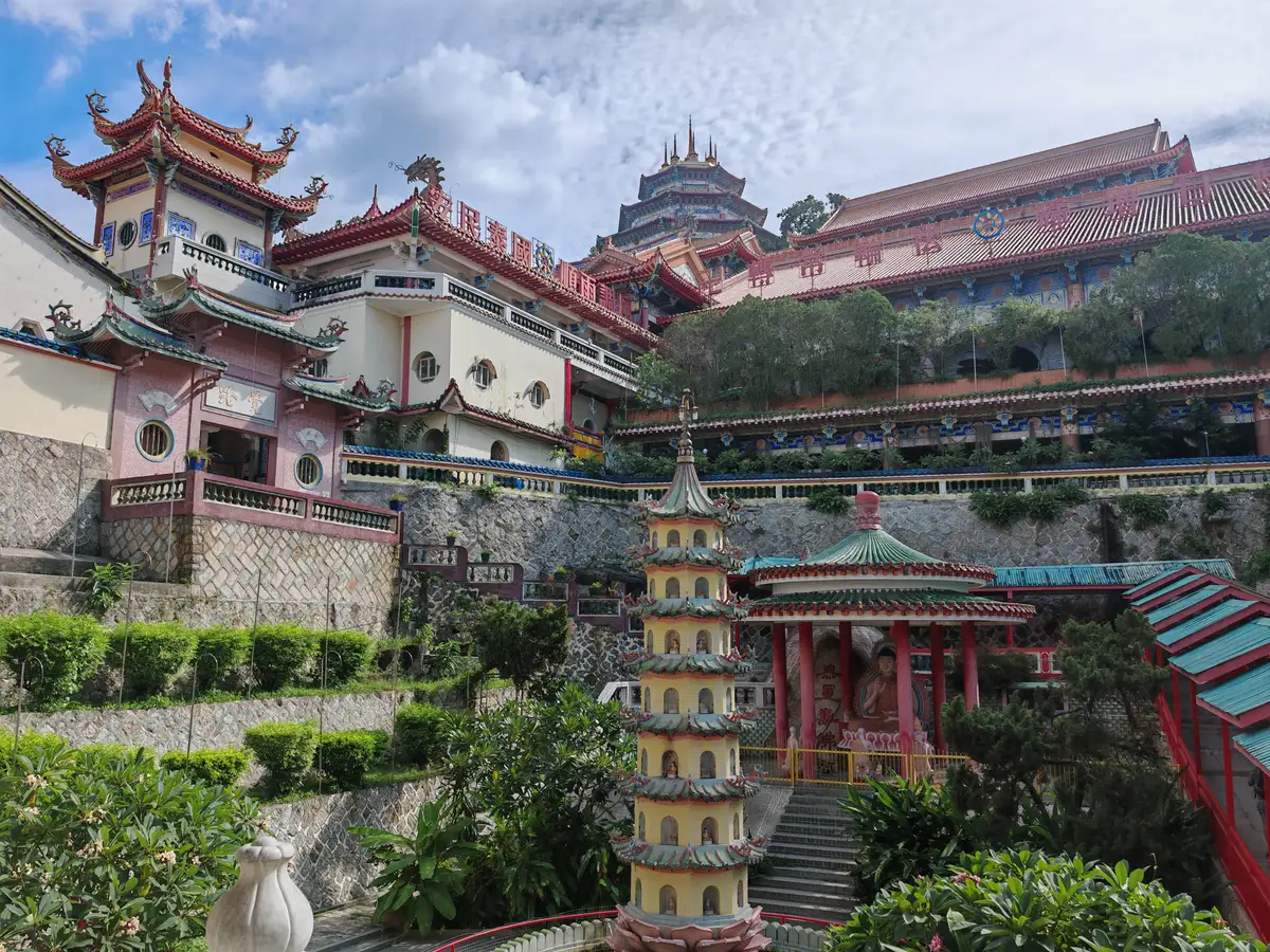 Colorful tiered roofs, a small lotus-style pagoda and a red pavilion with a seated Buddha figure at Kek Lok Si Temple on its Penang hillside