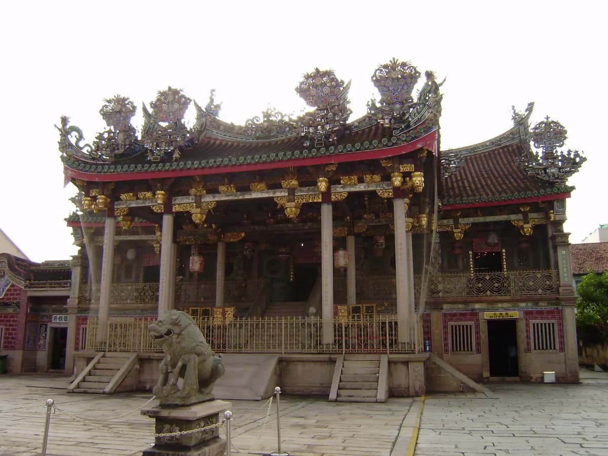 The ornate front of Khoo Kongsi clan house in George Town, with a carved and tiled roof, gilded beams, a stone lion and a paved courtyard
