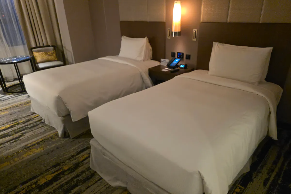 A tidy hotel room in Malaysia with two made-up single beds, a bedside lamp and curtained windows
