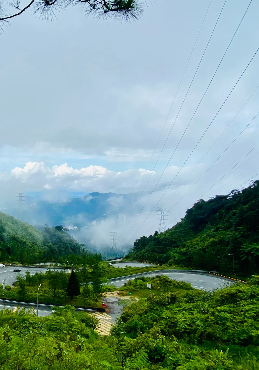 Mist drifting through forested hills above the winding mountain road that leads down from Genting Highlands, with layers of blue ridges behind