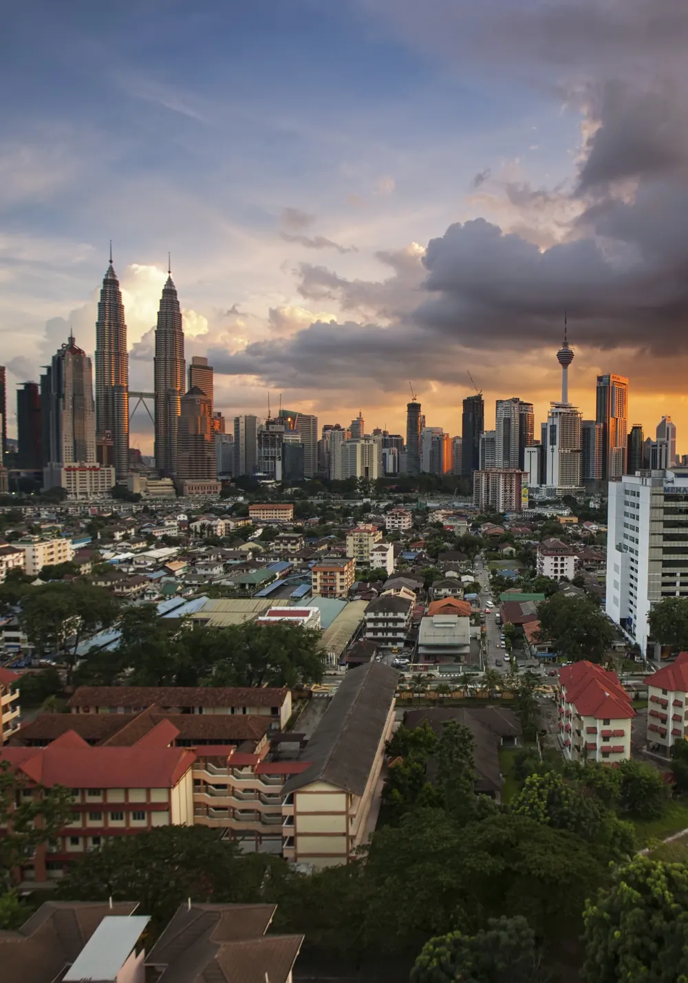 Dusk over Kuala Lumpur: the Petronas Twin Towers and KL Tower stand out from the city skyline while a storm cloud glows orange above the rooftops of the surrounding neighbourhoods