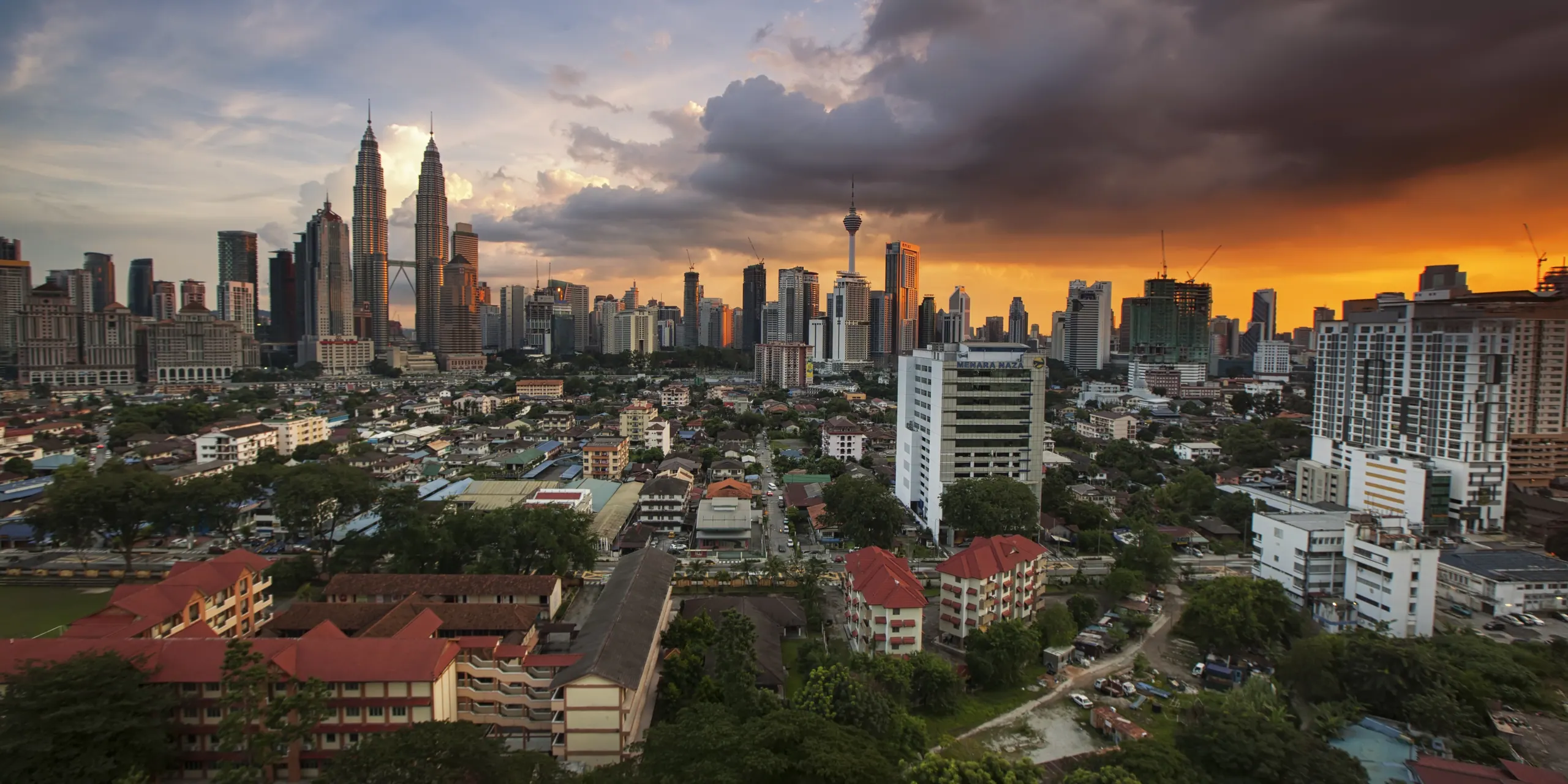 Dusk over Kuala Lumpur: the Petronas Twin Towers and KL Tower stand out from the city skyline while a storm cloud glows orange above the rooftops of the surrounding neighbourhoods